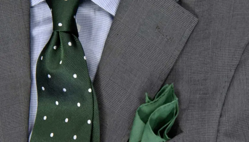 Elegancki zestaw: niebieska koszula, zielony krawat w kropki i szara marynarka. Idealna odpowiedź na pytanie: jaki krawat do niebieskiej koszuli.