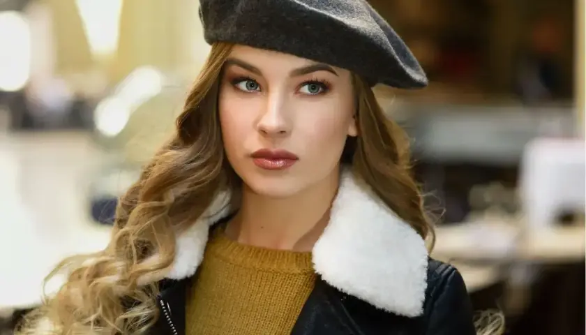 Elegancka kobieta w grafitowym beretu damskim, z burzą blond loków i w skórzanej kurtce. Inspiracja, jak nosić beret damski.