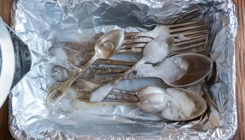 Srebrne sztućce z czarnym nalotem wkładane do folii aluminiowej, zalewane gorącą wodą z solą.