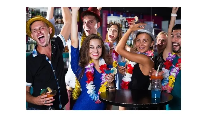 Grupa przyjaciół świętuje w klubie w stylu hawajskim, z kolorowymi girlandami i drinkami.