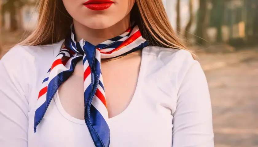 Kobieta w białej koszuli i apaszce w paski. Dowiedz się, jak nosić apaszkę do koszuli, by wyglądać stylowo.