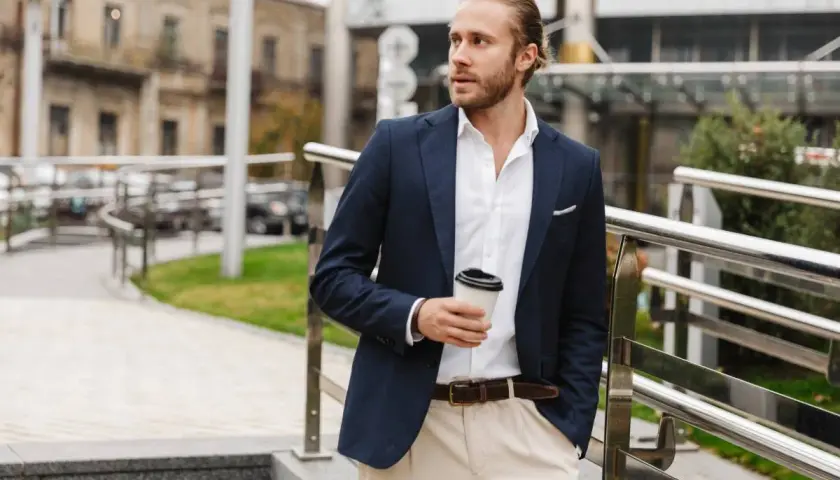 Mężczyzna w stylu smart casual z kawą w ręku, ubrany w granatową marynarkę i jasne spodnie, idzie po schodach.