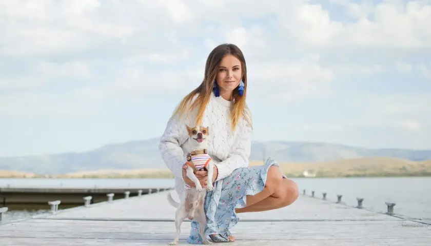 Dziewczyna w swetrze i kwiecistej sukience, z chihuahuą na rękach, prezentuje swój letni styl ubierania na tle jeziora.