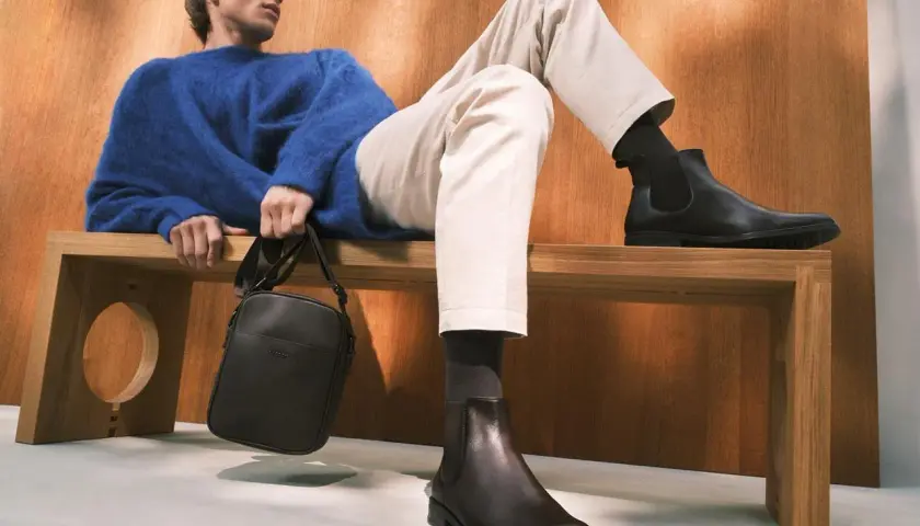 Eleganckie, ciemne botki to idealne buty do chinosów i koszuli. Mężczyzna w niebieskim swetrze prezentuje stylowy zestaw.
