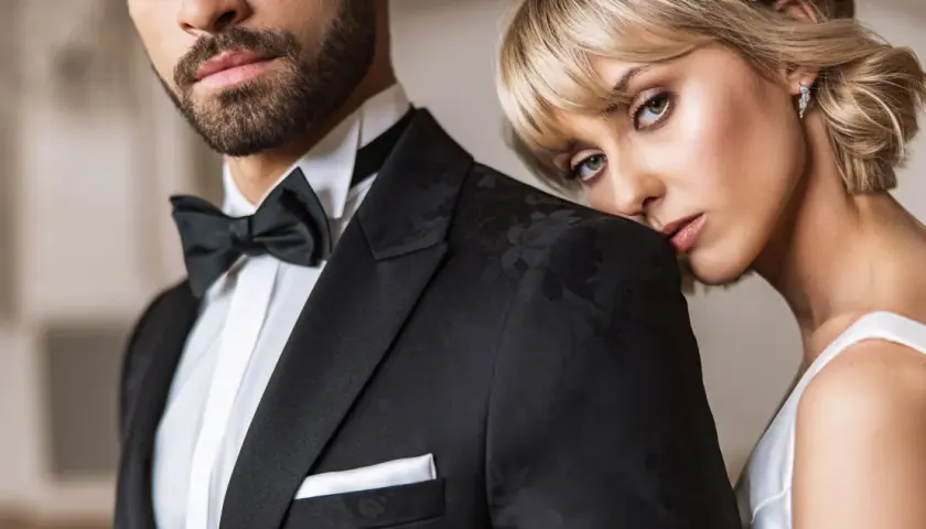 Elegancki mężczyzna w czarnym smokingu z muchą i białą koszulą. Kobieta opiera głowę na jego ramieniu. Idealny przykład, jaka koszula do muchy.