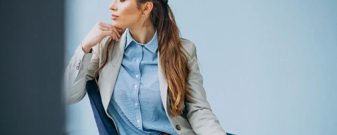 Elegancka kobieta w jasnej marynarce i błękitnej koszuli męskiej, tworząca stylową, biznesową stylizację.