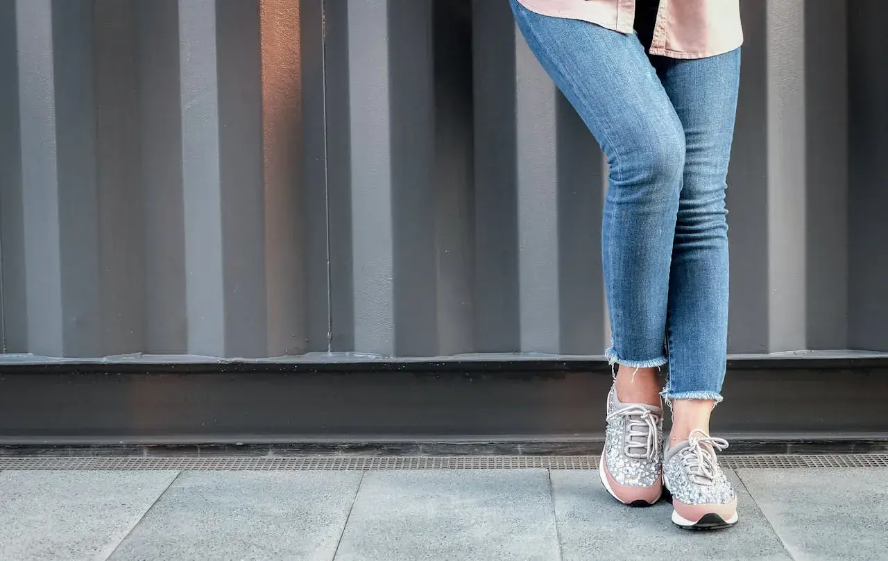 Nogawki jeansów postrzępione na dole, modne sneakersy z błyszczącymi detalami.
