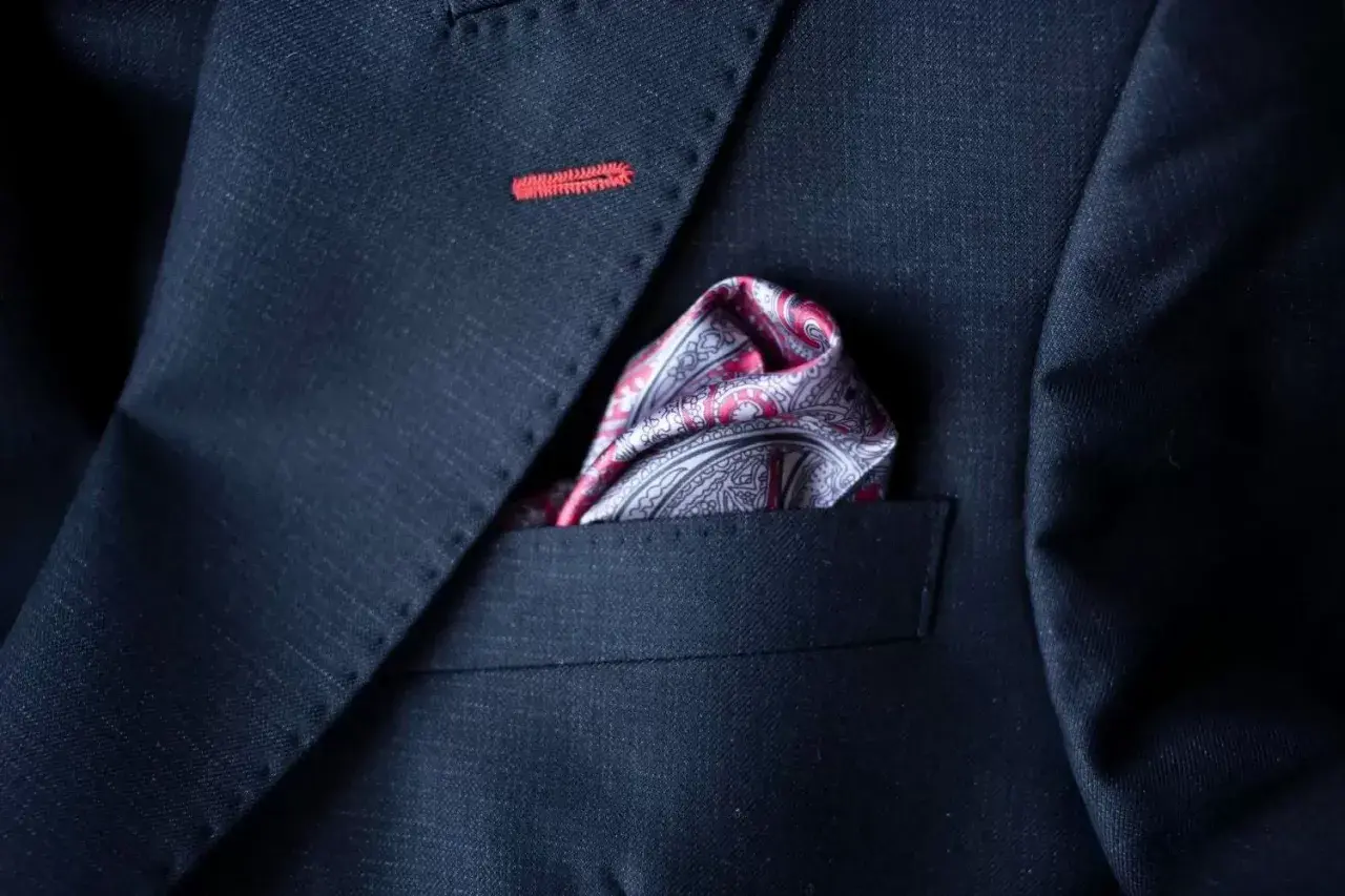 Elegancka poszetka w paisley do granatowego garnituru, z subtelnym czerwonym przeszyciem na klapie.