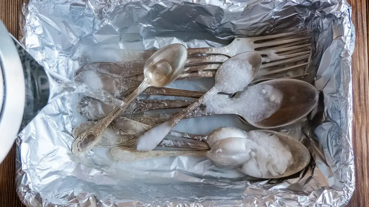 Srebrne sztućce z czarnym nalotem wkładane do folii aluminiowej, zalewane gorącą wodą z solą.