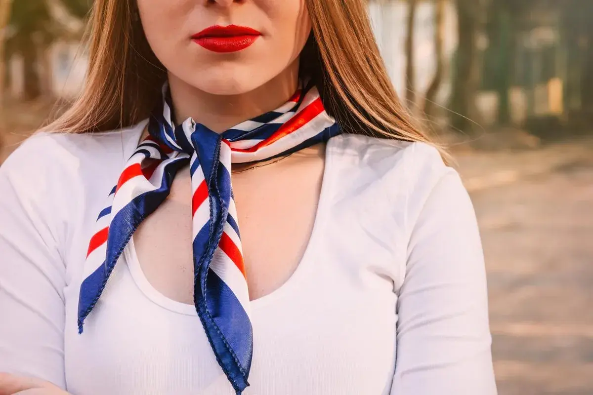 Kobieta w białej koszuli i apaszce w paski. Dowiedz się, jak nosić apaszkę do koszuli, by wyglądać stylowo.