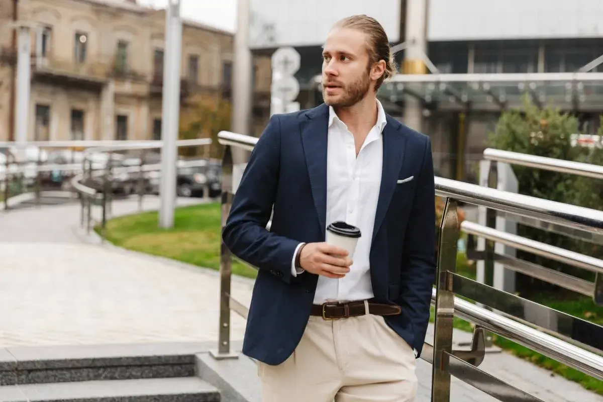Mężczyzna w stylu smart casual z kawą w ręku, ubrany w granatową marynarkę i jasne spodnie, idzie po schodach.