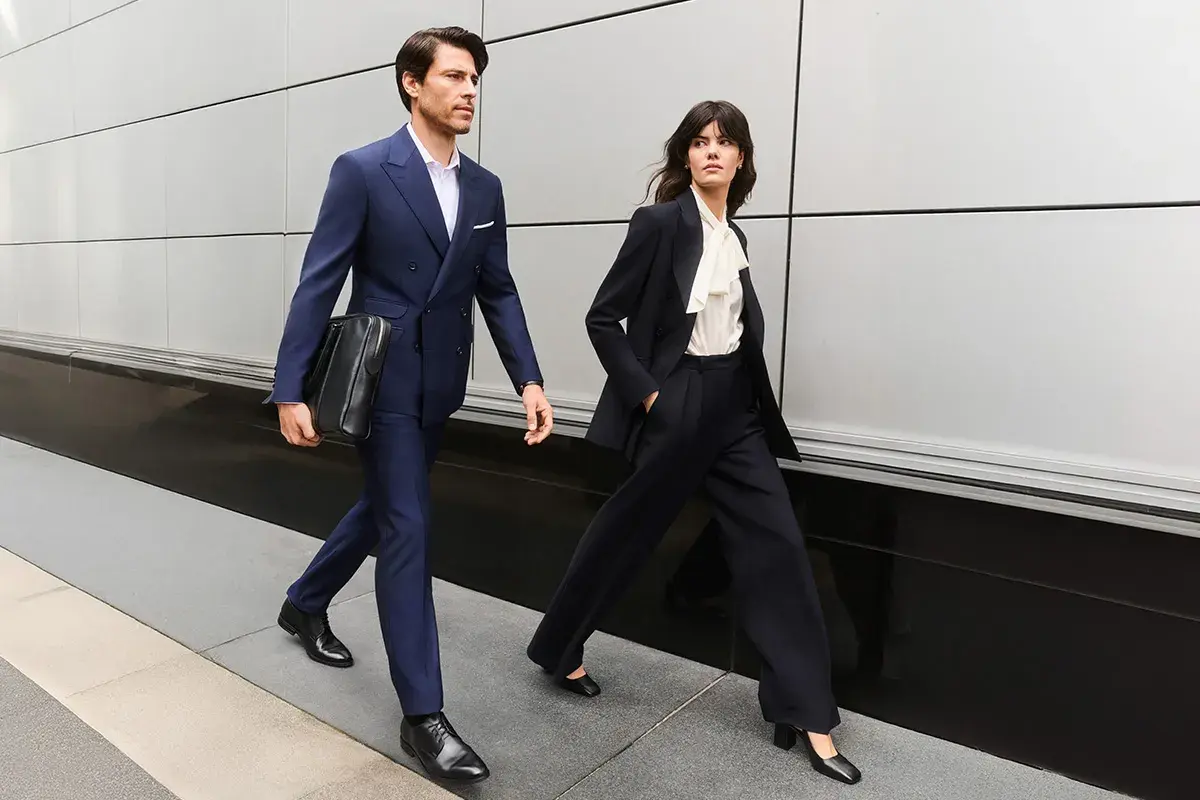 Para idąca w stylu business formal. Mężczyzna w granatowym garniturze, kobieta w ciemnym.