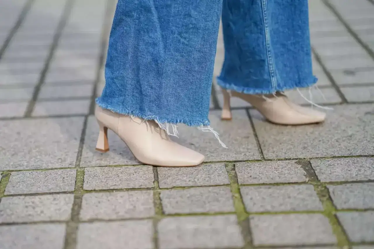 Nogawki jeansów postrzępione na dole, w połączeniu z beżowymi botkami na obcasie, tworzą modny, miejski look.