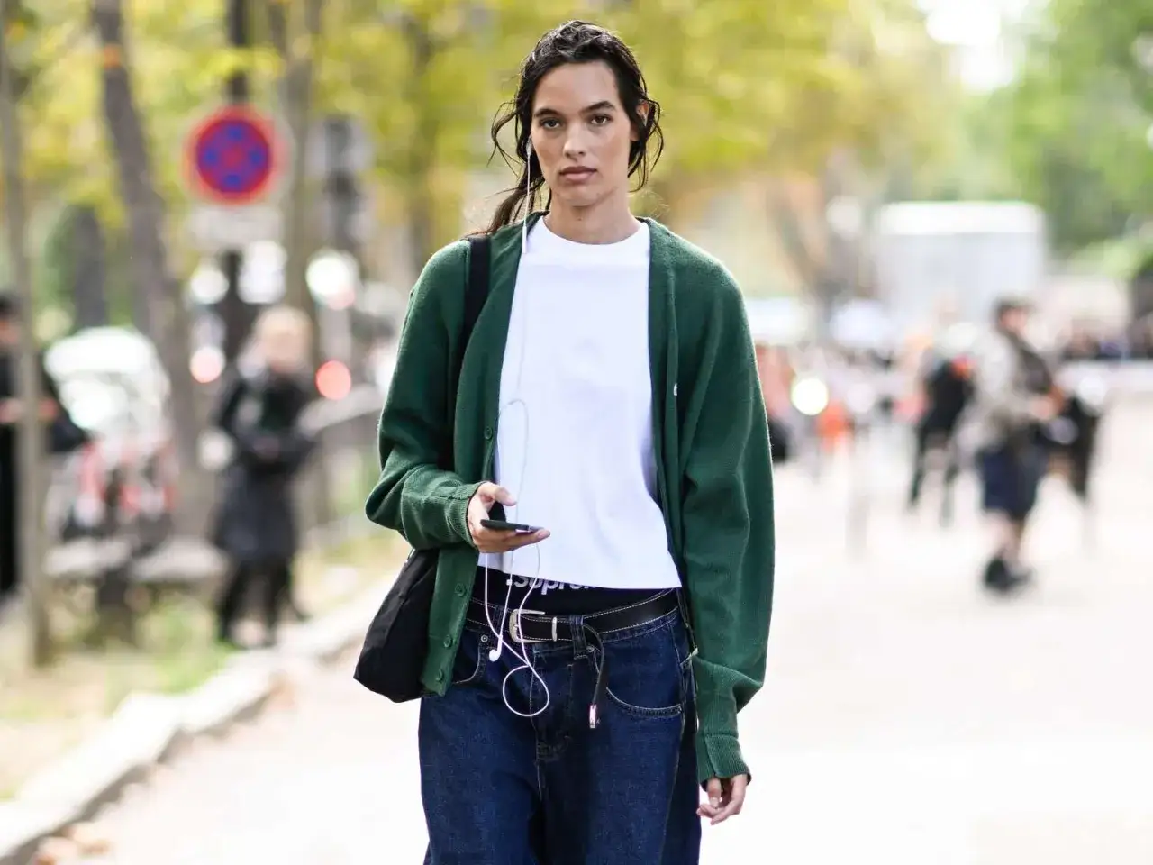 Kobieta w zielonym kardiganie, białej koszulce i jeansach prezentuje styl normcore.