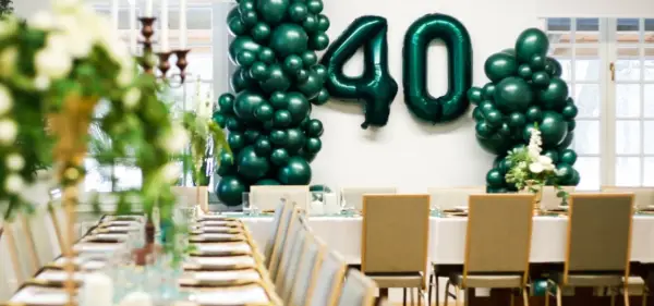 Uroczyste przyjęcie z okazji 40 urodzin w stylu lat 80. Zielone balony tworzą łuk z liczbą 40. Stoły nakryte do kolacji.